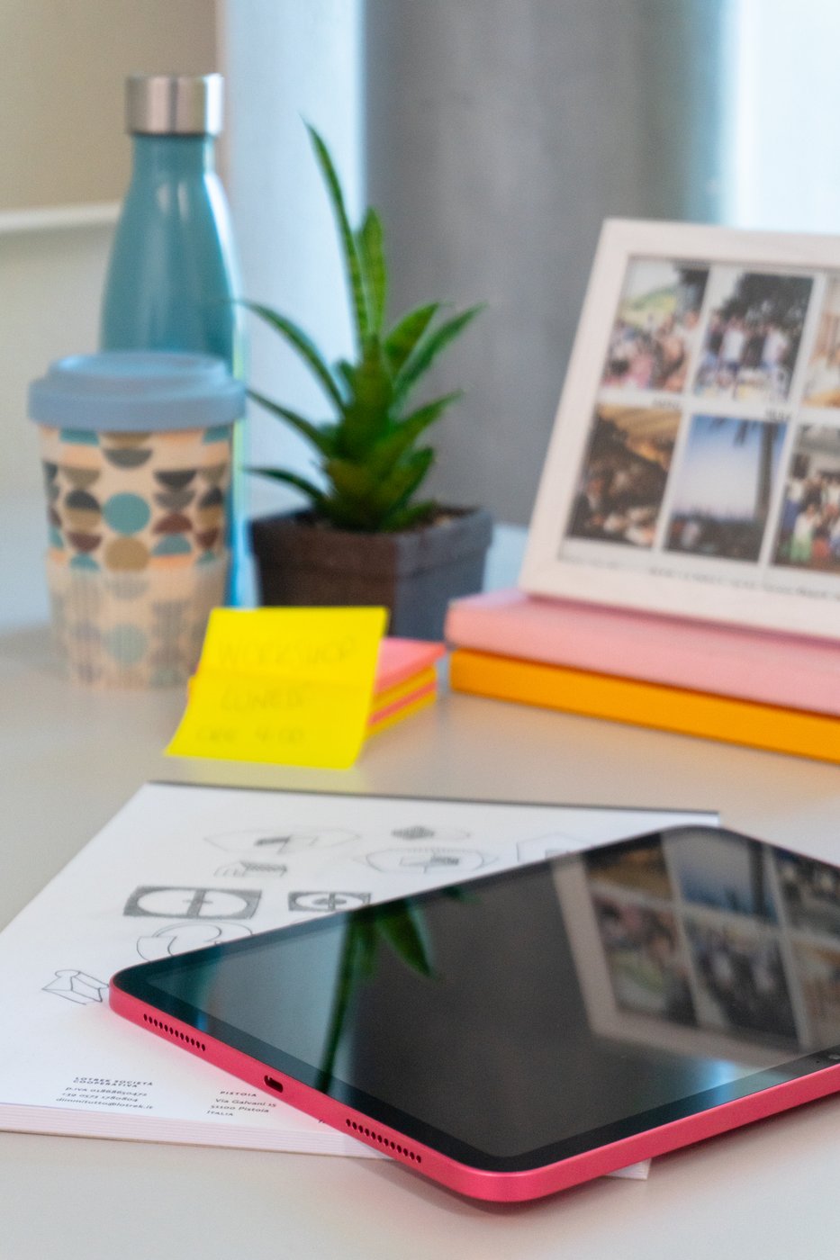 Scrivania con tablet, tazza, borraccia, pianta e foto incorniciata.