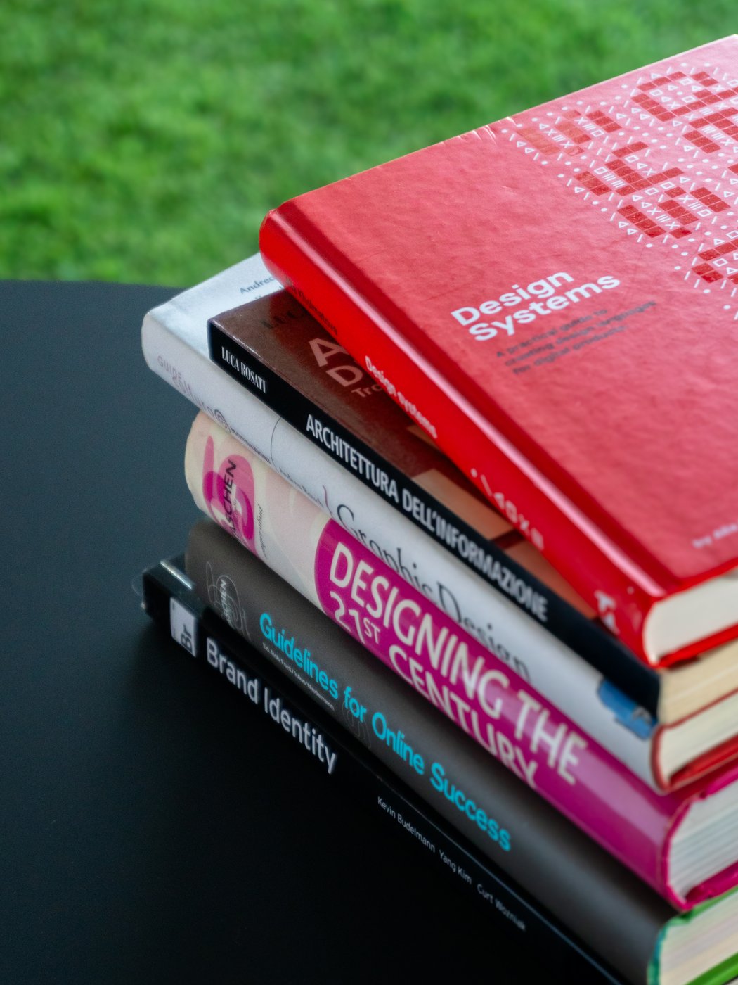 Pile di libri su bancone nero con sfondo verde, tra cui Design Systems e Brand Identity.