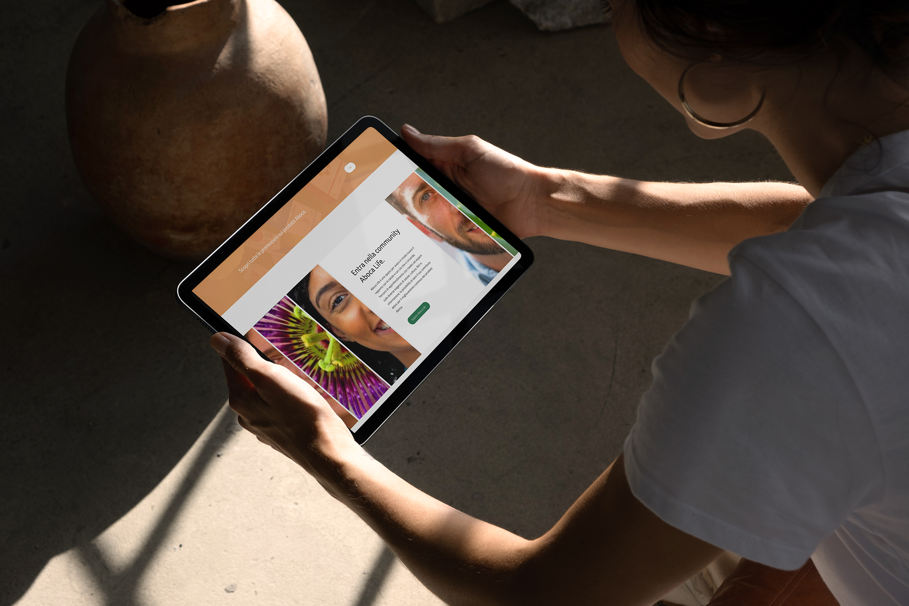 Donna osserva un tablet con il sito web di Aboca Life, mostrando volti e un fiore.