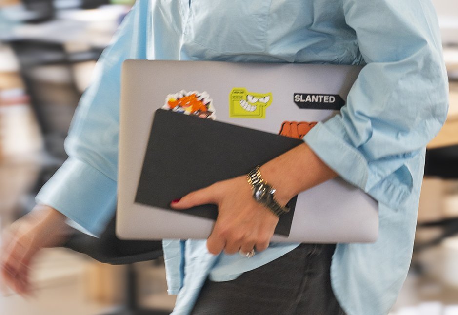 Uomo con barba e maglietta bianca legge un libro rosso in una libreria, con piante.