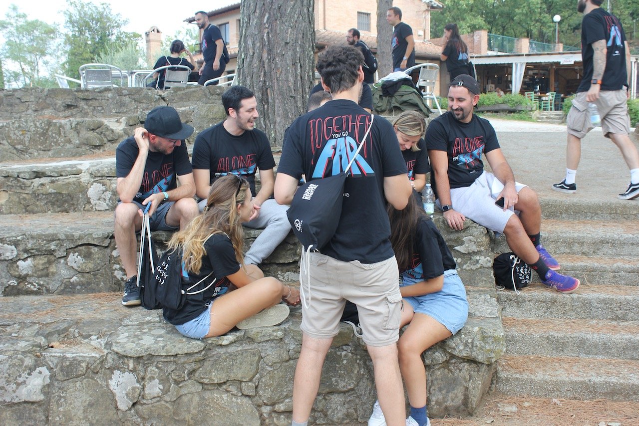 Gruppo di persone sedute su gradini di pietra, molti indossano magliette nere con logo 'Together for Fair'.