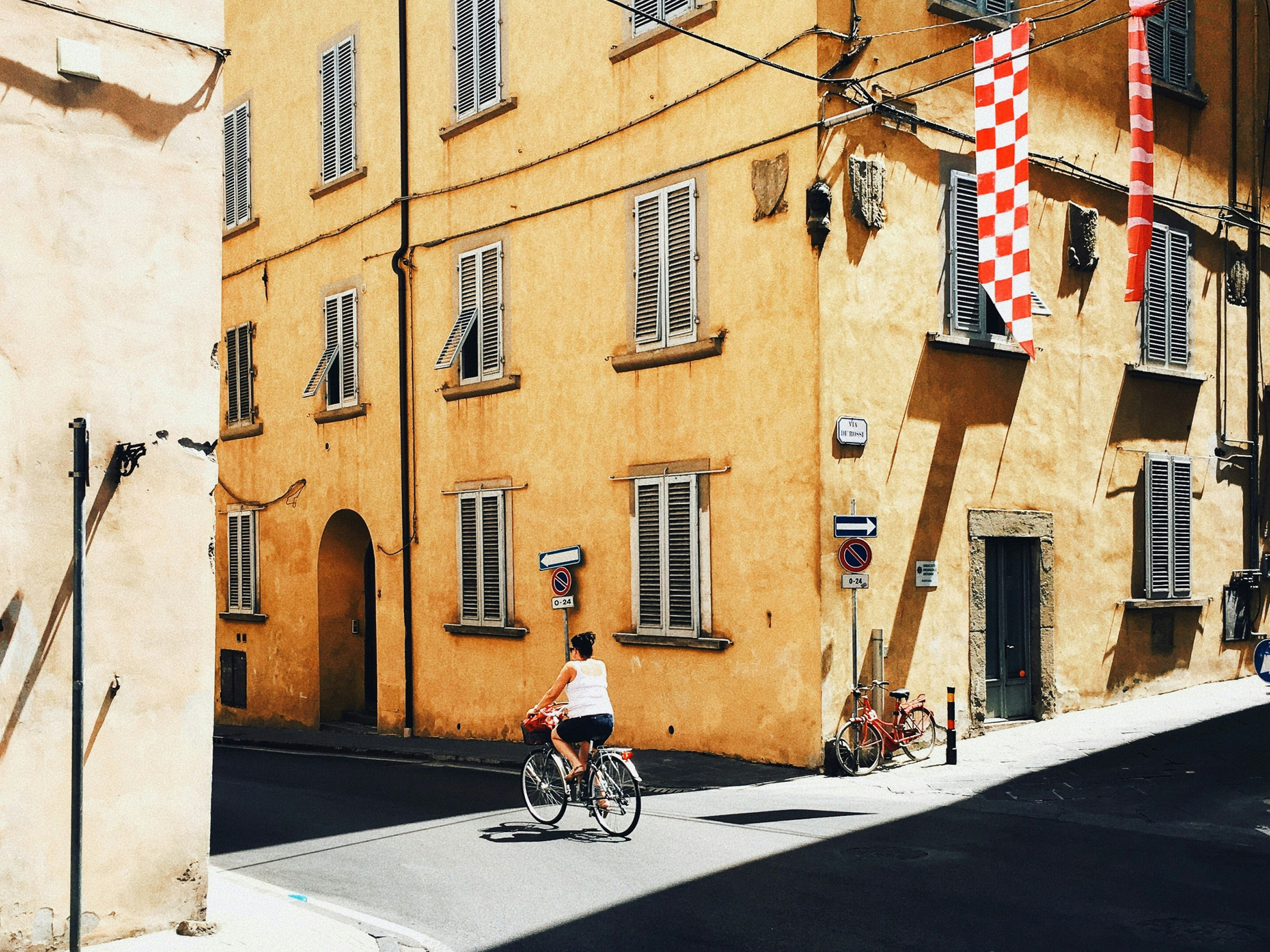 Donna in bicicletta percorre una strada di fronte a un edificio giallo.