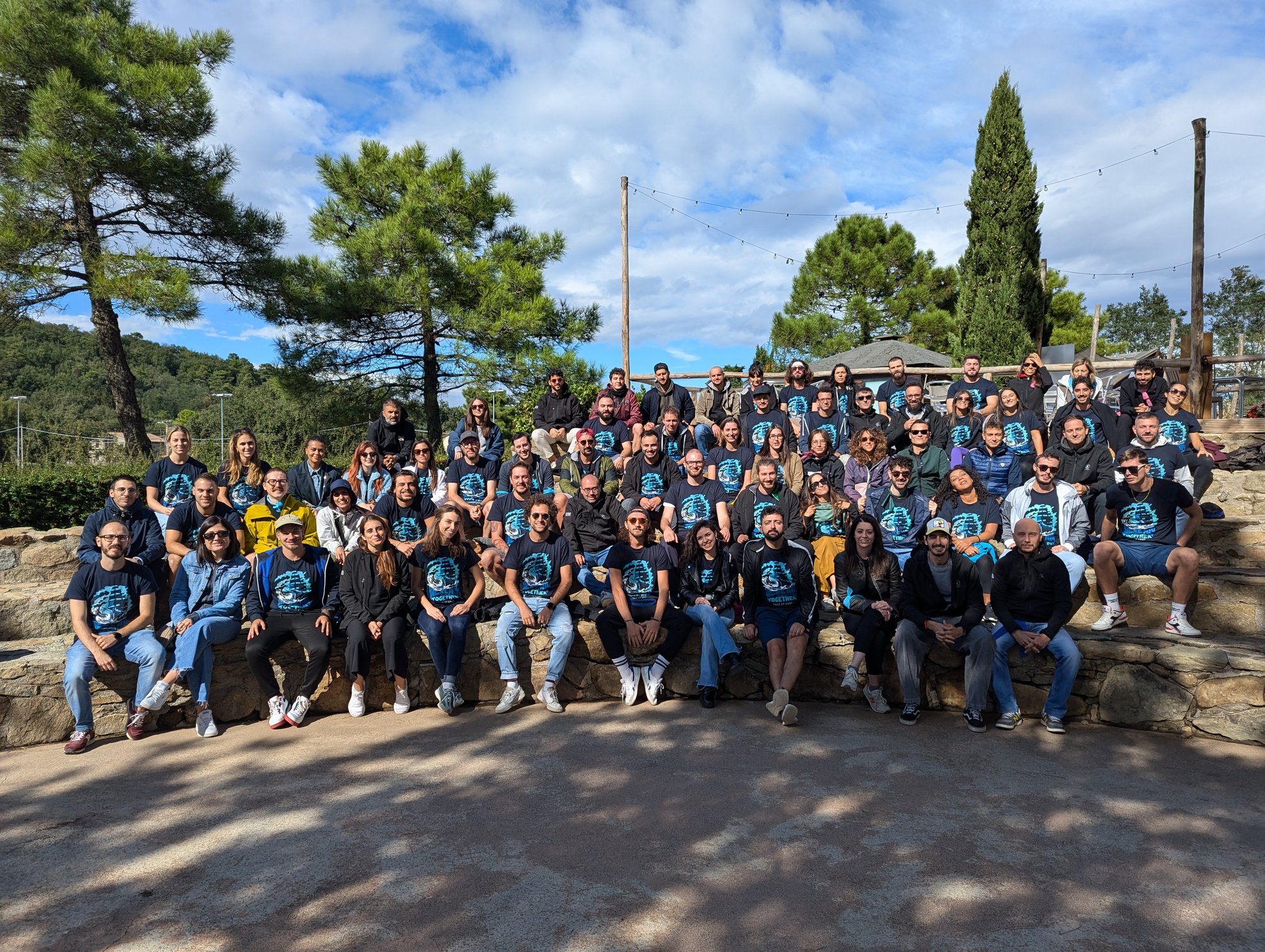 Ampio gruppo di persone sedute su gradini di pietra all'aperto, quasi tutti con magliette blu.