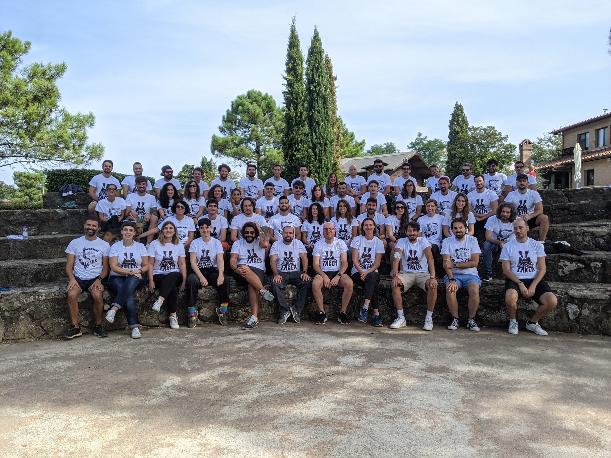 Gruppo di persone sedute su gradini di pietra, quasi tutti indossano magliette bianche.