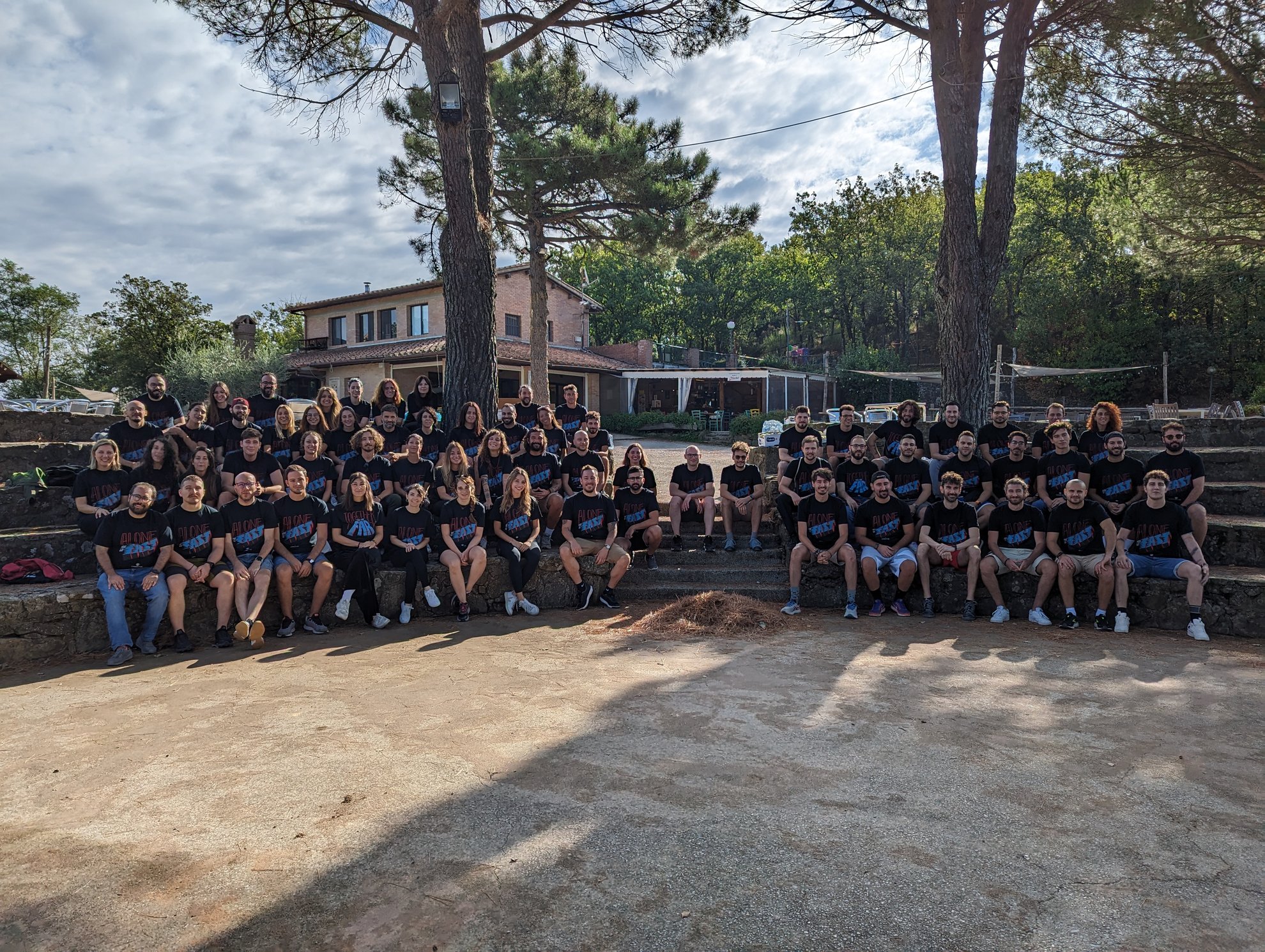 Grande gruppo di persone sedute su gradini di cemento all'aperto, molti indossano magliette nere.