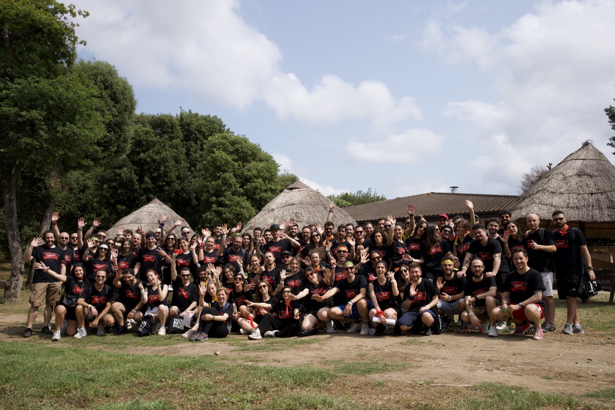Grande folla di persone in piedi e sedute posa per una foto di gruppo, molti con magliette nere.